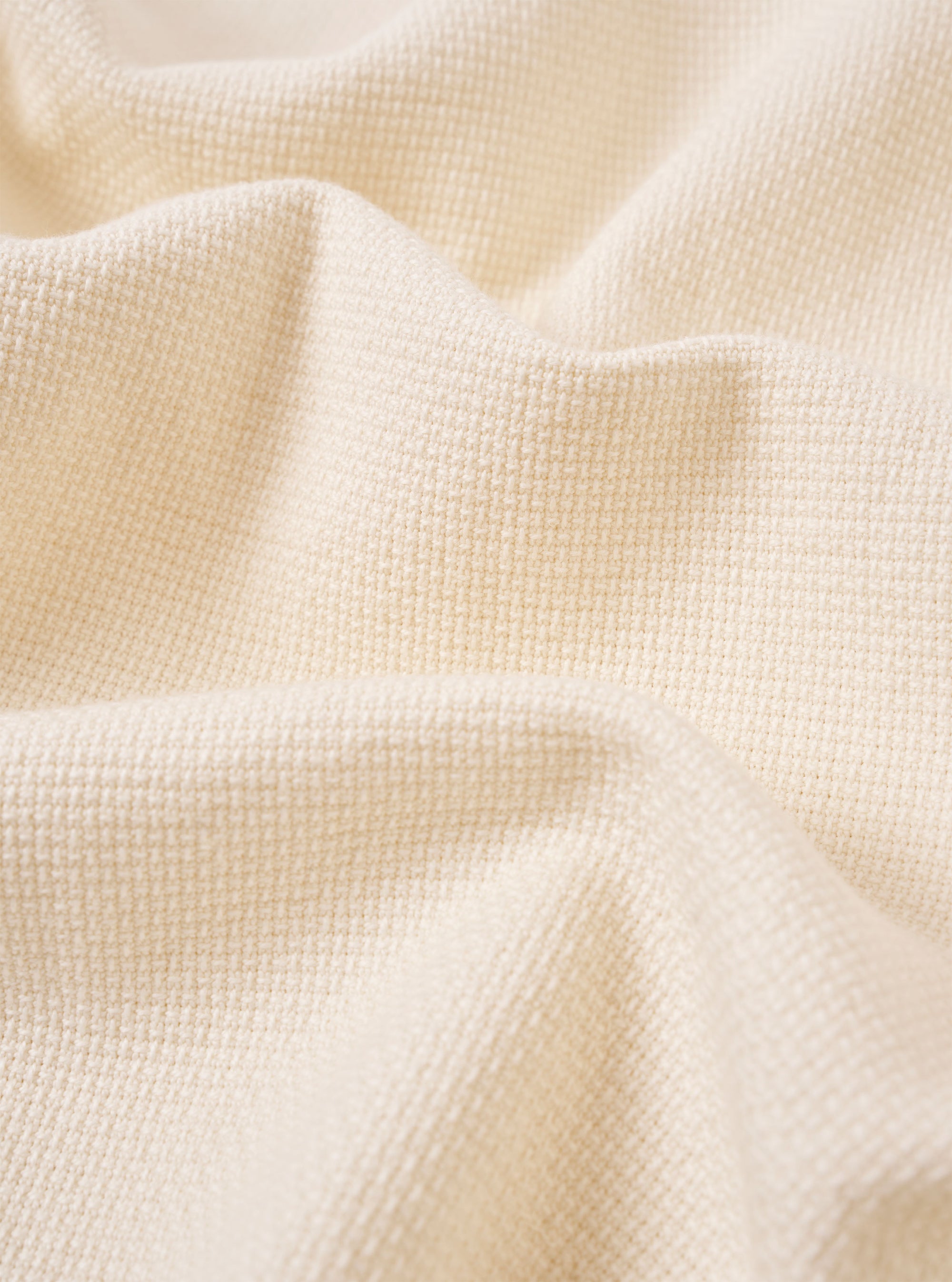 A close-up fabric swatch of the Ecru Kendal Cotton Travail Overshirt highlights the off-white, ecru color and the substantial, open-weave texture of the cotton fabric. The material fills the frame, providing a detailed view of the garment's weave and construction.