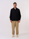 The Black Kendal Cotton Travail Overshirt is presented as a flat lay against a plain white background. The overshirt features a one-piece collar, a central button-down closure, and two large patch pockets at the waist. The black cotton fabric has a distinct textured appearance. The garment is finished with a curved hem and subtle chest darts.