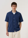 The Blue Maui Cotton Road Shirt is worn by a model against a plain white background. The shirt features a vertical striped pattern in blue and navy, a camp collar, and a single chest pocket on the left side. The model is shown from the chest up, with the shirt buttoned.