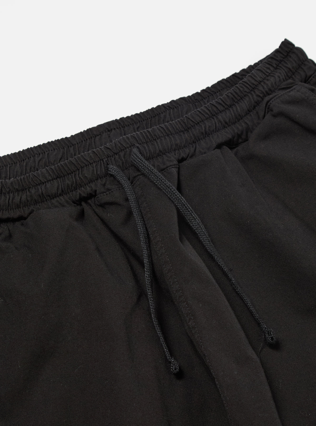 The Black Kelly Cotton Simple Short is shown from the back as a flat lay against a plain white background. The shorts feature an elasticated waistband and a single patch pocket on the right rear side. The fabric is a solid black cotton with visible stitching details.
