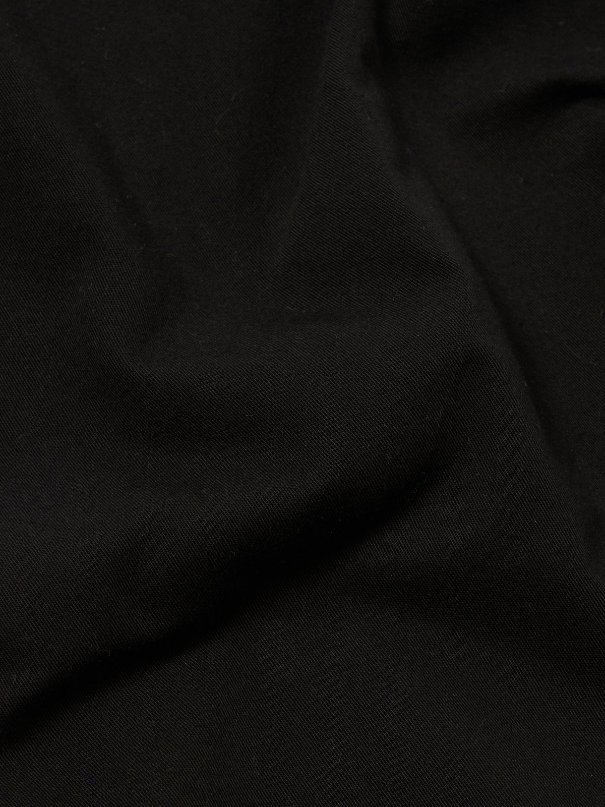 A close-up fabric swatch of the Black Kelly Cotton Simple Short highlights the solid black color and the smooth, fine texture of the cotton material. The fabric fills the frame, providing a detailed view of the weave and finish.
