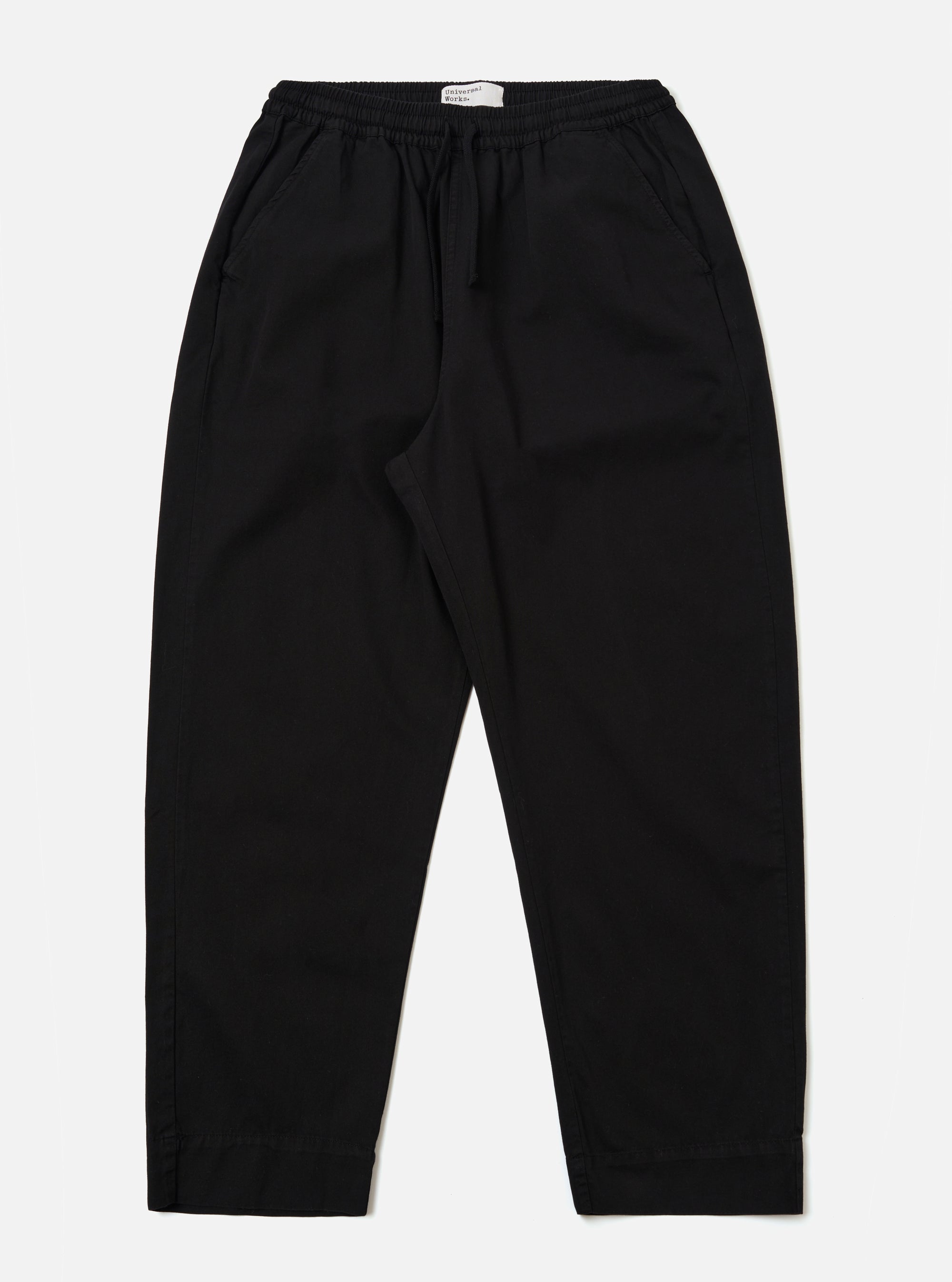 The Black Kelly Cotton Judo Pant is shown as a flat lay against a plain white background. The trousers feature a straight, wide-leg silhouette with an elasticated waistband and a visible tonal drawstring. Two side pockets are prominent at the hips. The fabric appears sturdy with a smooth finish.