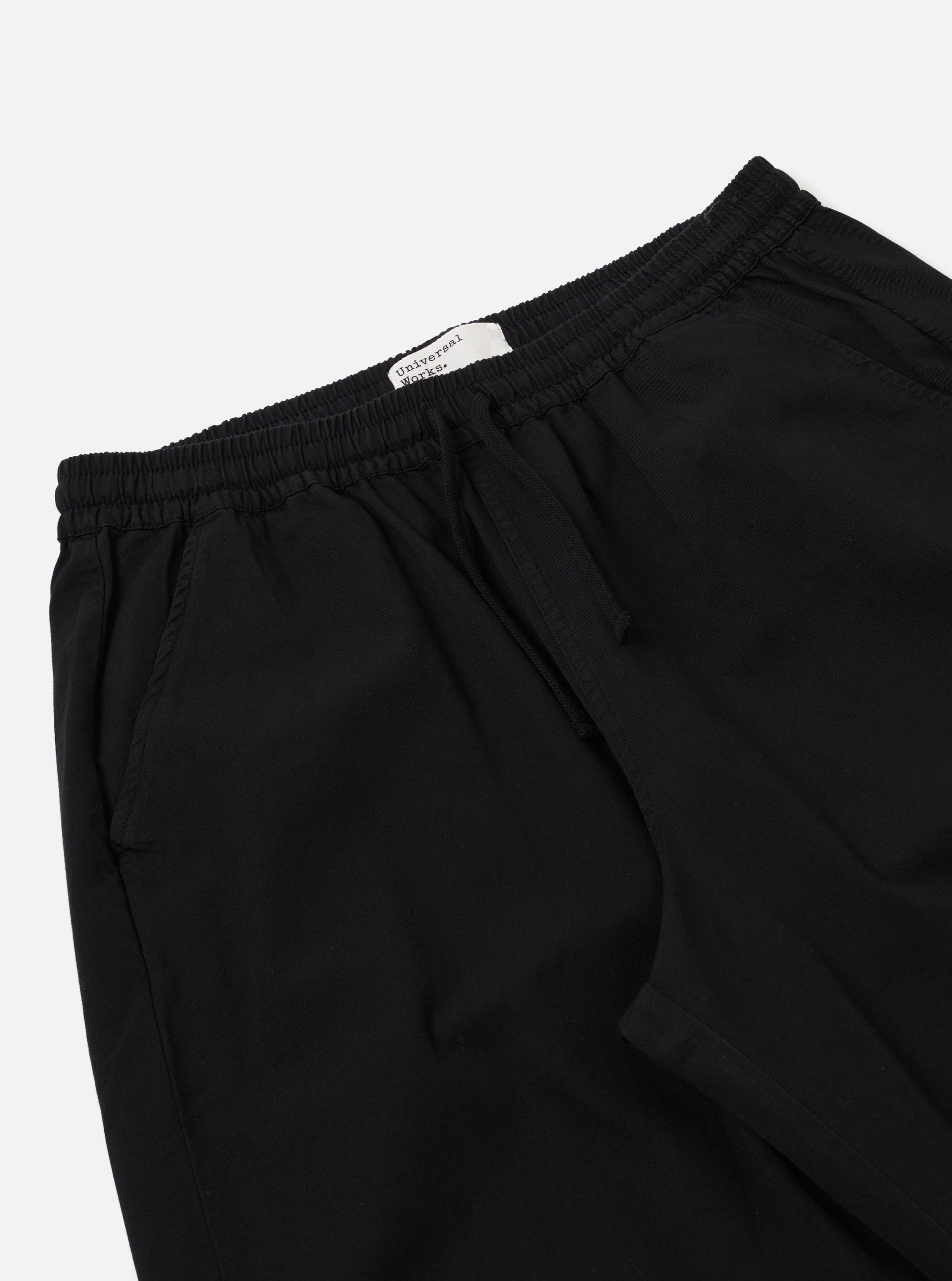 The Black Kelly Cotton Judo Pant is shown from a rear three-quarter angle as a flat lay against a white background. This view highlights the simple, straight-leg construction and the single rear patch pocket on the right side. The elasticated waistband and the absence of a traditional fly are clearly visible.