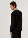 A model wears the Black Kelly Cotton Glider Jacket against a plain white background. The jacket is a collarless, zip-front utility style with bound edges and four prominent 3D bellows pockets on the front. The model is shown from the torso up, paired with a white t-shirt, emphasizing the jacket's regular fit and the dry, slightly polished texture of the Kelly Cotton twill fabric.