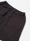 The Licorice Lyo Linen Mix Simple Short is displayed as a flat lay against a plain white background. The shorts feature an elasticated waistband with an internal drawstring, two side pockets, and a single rear buttoned flap pocket. The fabric has a textured appearance and is a dark licorice brown color.
