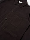 The Licorice Lyo Linen Mix Coverall Jacket is shown from a rear three-quarter angle as a flat lay against a plain white background. The image highlights the jacket's short, boxy silhouette, the straight hem, and the simple, unbuttoned cuffs. The dark brown fabric has a smooth, slightly washed appearance.