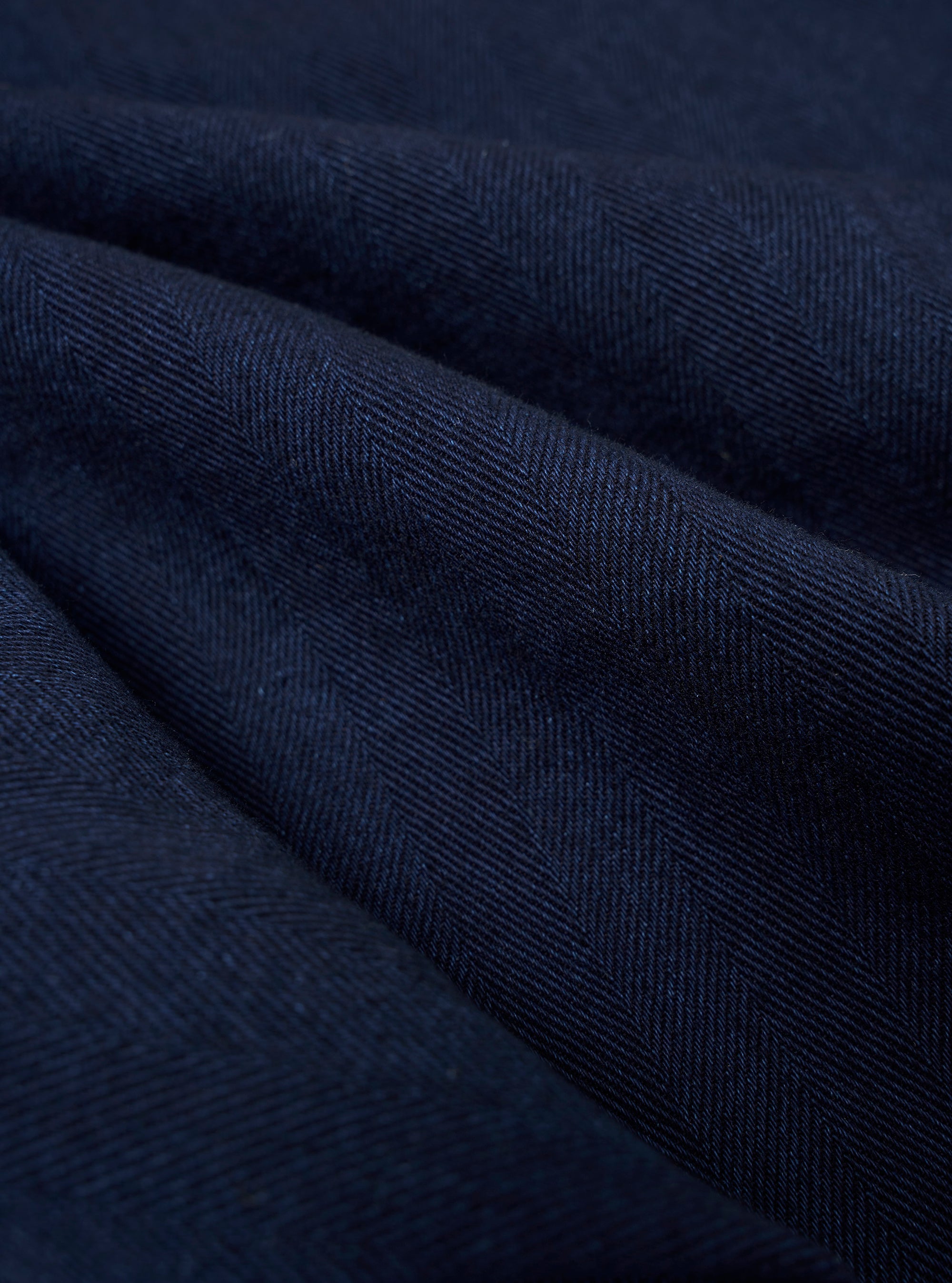 A close-up fabric swatch of the Indigo Recycled Herringbone Pleated Track Short displays the blue and white herringbone weave pattern.