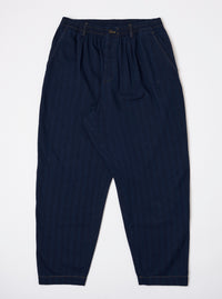 The Indigo Recycled Herringbone Pleated Track Pant is shown as a flat lay against a plain white background. The trousers feature a drawstring waistband, a single pleat on each leg, and a relaxed, tapered fit. The dark indigo fabric has a visible herringbone texture.