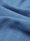 A close-up swatch image of the Washed Indigo Recycled Herringbone Pleated Track Pant fabric highlights the blue washed indigo color and the distinct V-shaped herringbone weave. The textured recycled cotton material fills the frame, providing a detailed view of the garment's textile construction.