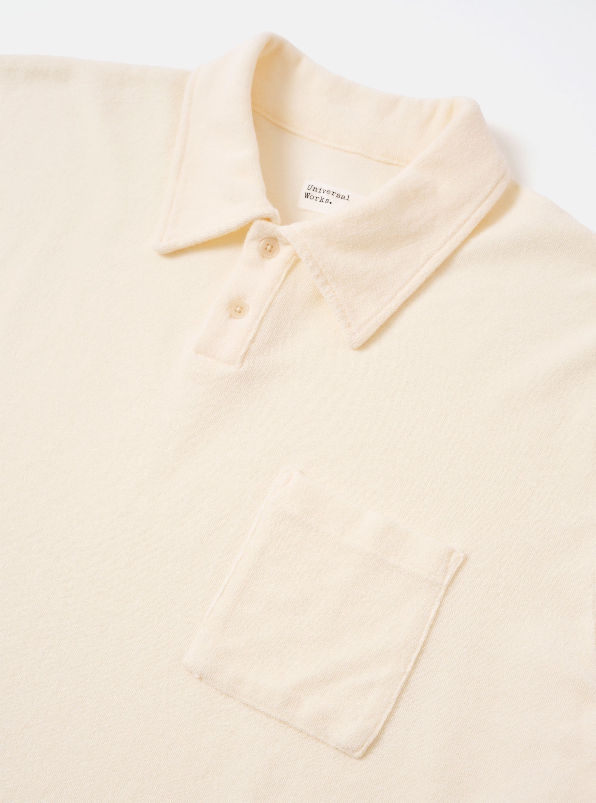 The Ecru Light Weight Terry Newlyn Polo is shown from the back as a flat lay against a plain white background. The garment features a simple, clean-cut back panel, short sleeves, and a structured polo collar. The fabric is an off-white ecru with a soft, looped terry texture.
