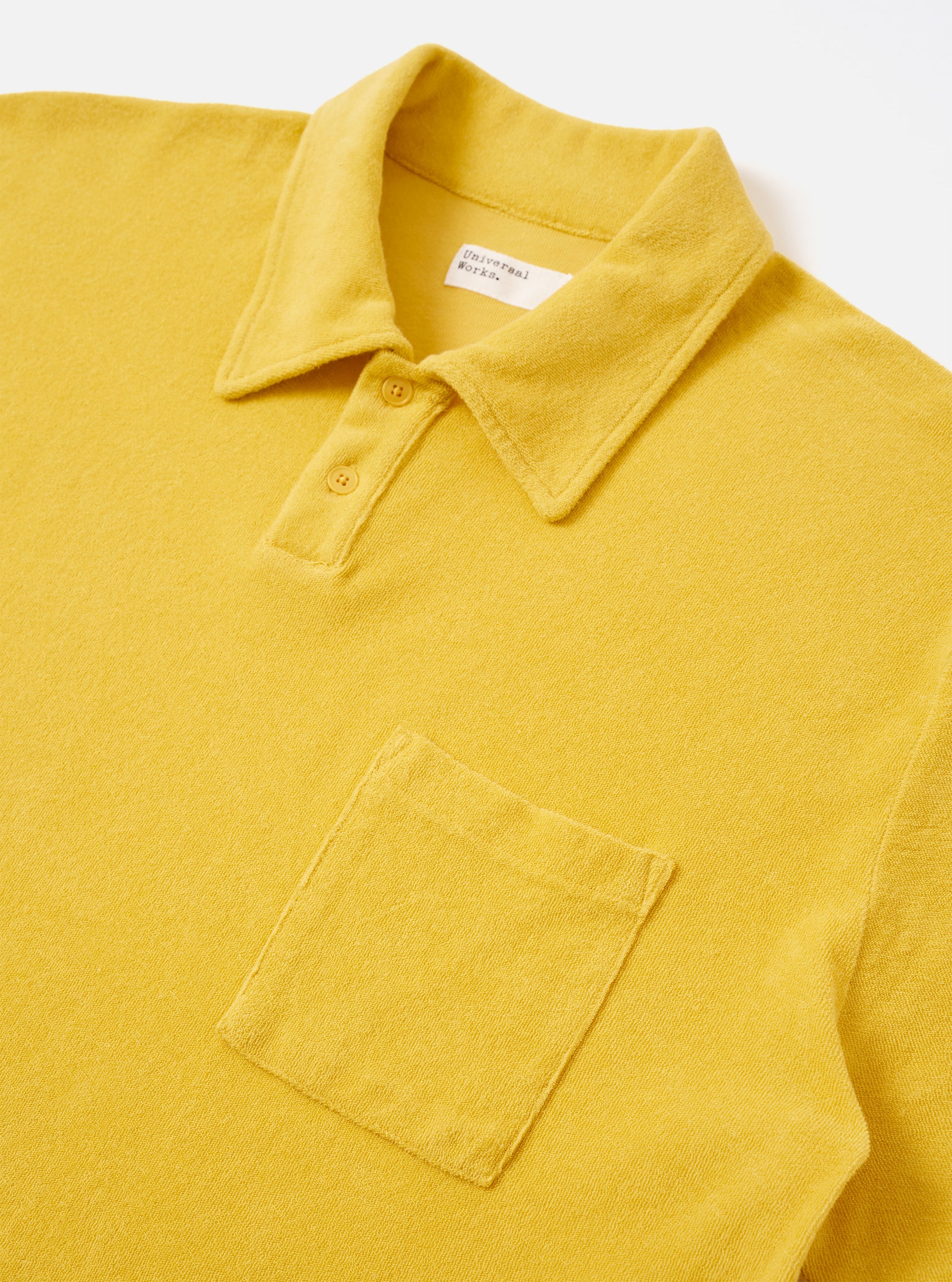 The Yellow Light Weight Terry Newlyn Polo is shown from a rear angle as a flat lay against a plain white background. The image highlights the soft, textured terry cotton fabric, the back of the collar, and the clean stitching along the hem and sleeves.