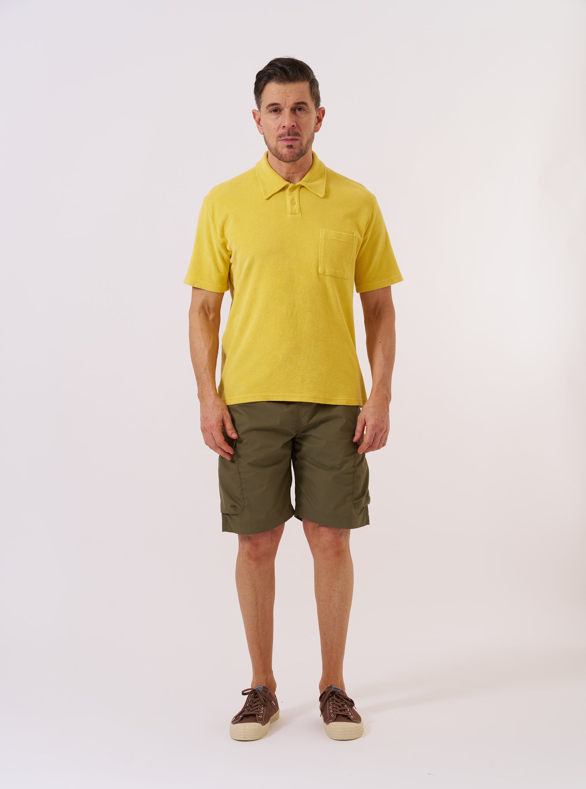 The Yellow Light Weight Terry Newlyn Polo is presented as a flat lay against a plain white background. The polo features a classic collar, a three-button placket, and short sleeves, crafted from a textured yellow light weight terry fabric.