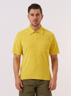 A model wears the Yellow Light Weight Terry Newlyn Polo while standing against a plain white background. The polo features a classic collar, a short button placket, and short sleeves. The garment is made from a vibrant yellow light weight terry fabric with a soft, textured appearance.