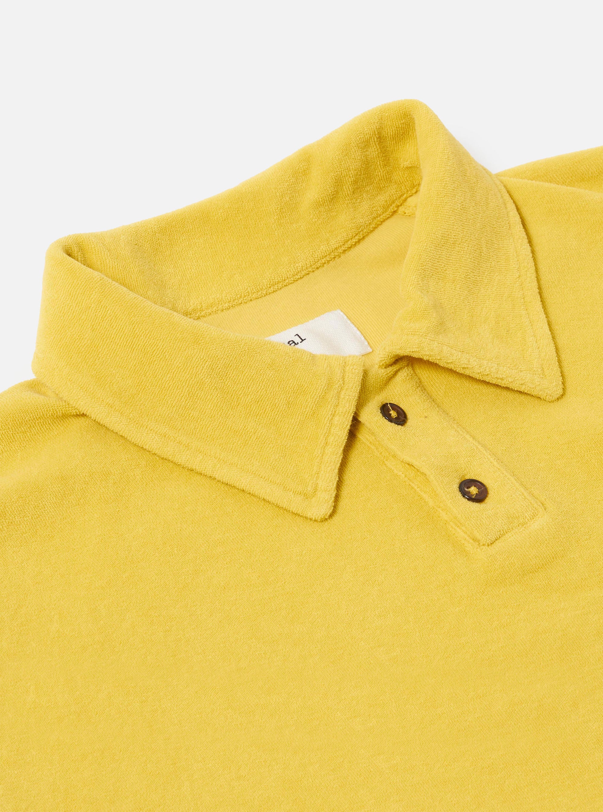 The Yellow Light Weight Terry Newlyn Polo is shown as a flat lay against a plain white background. The polo features a classic collar, a three-button placket, and short sleeves. The vibrant yellow-ochre fabric has a soft, visible looped terry texture.