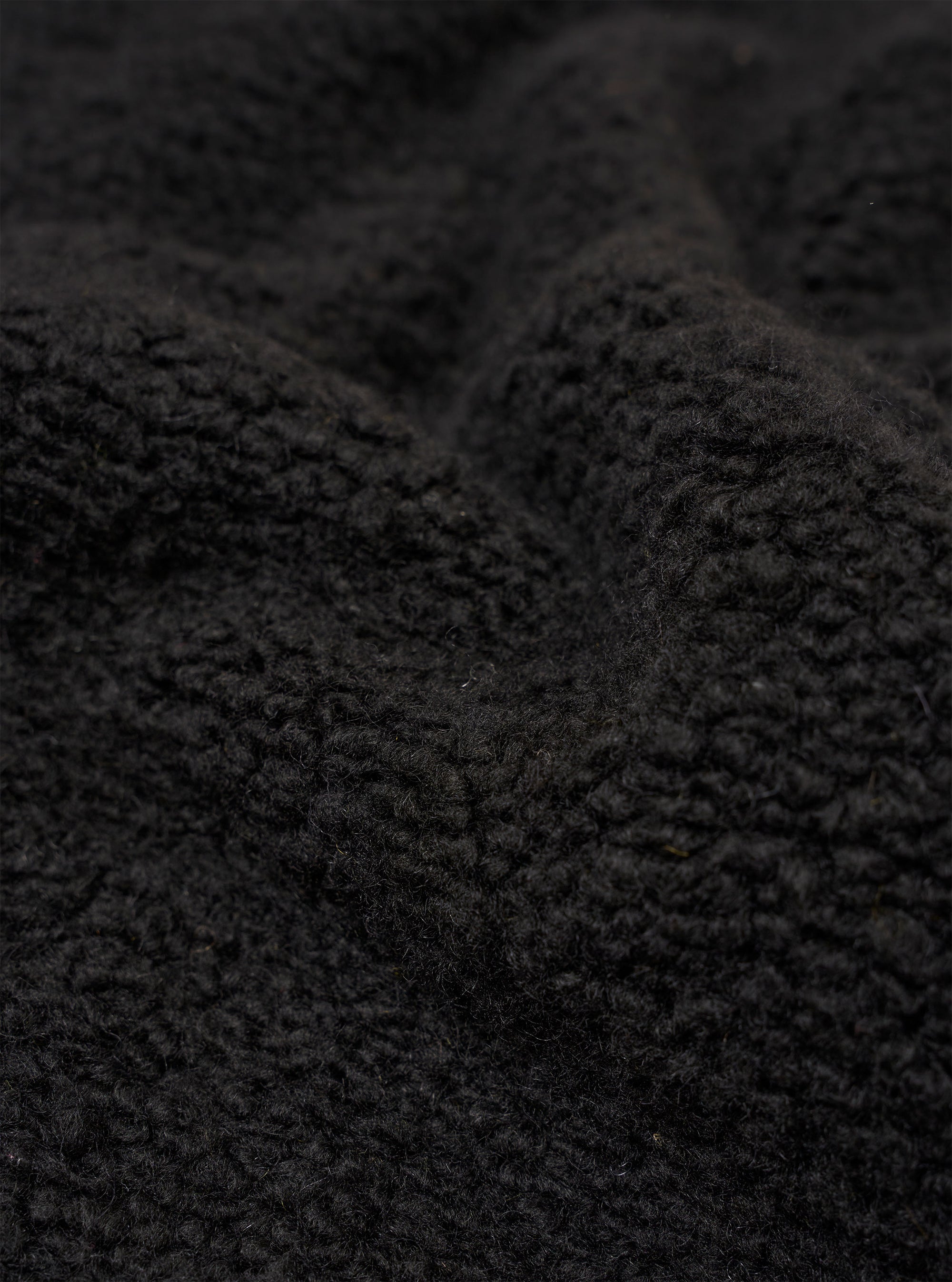 A close-up swatch image of the Black Alvar Fleece Lancaster Jacket highlights the thick, curly, and looped texture of the black fleece fabric. The material fills the entire frame, providing a detailed view of the garment's color and construction.