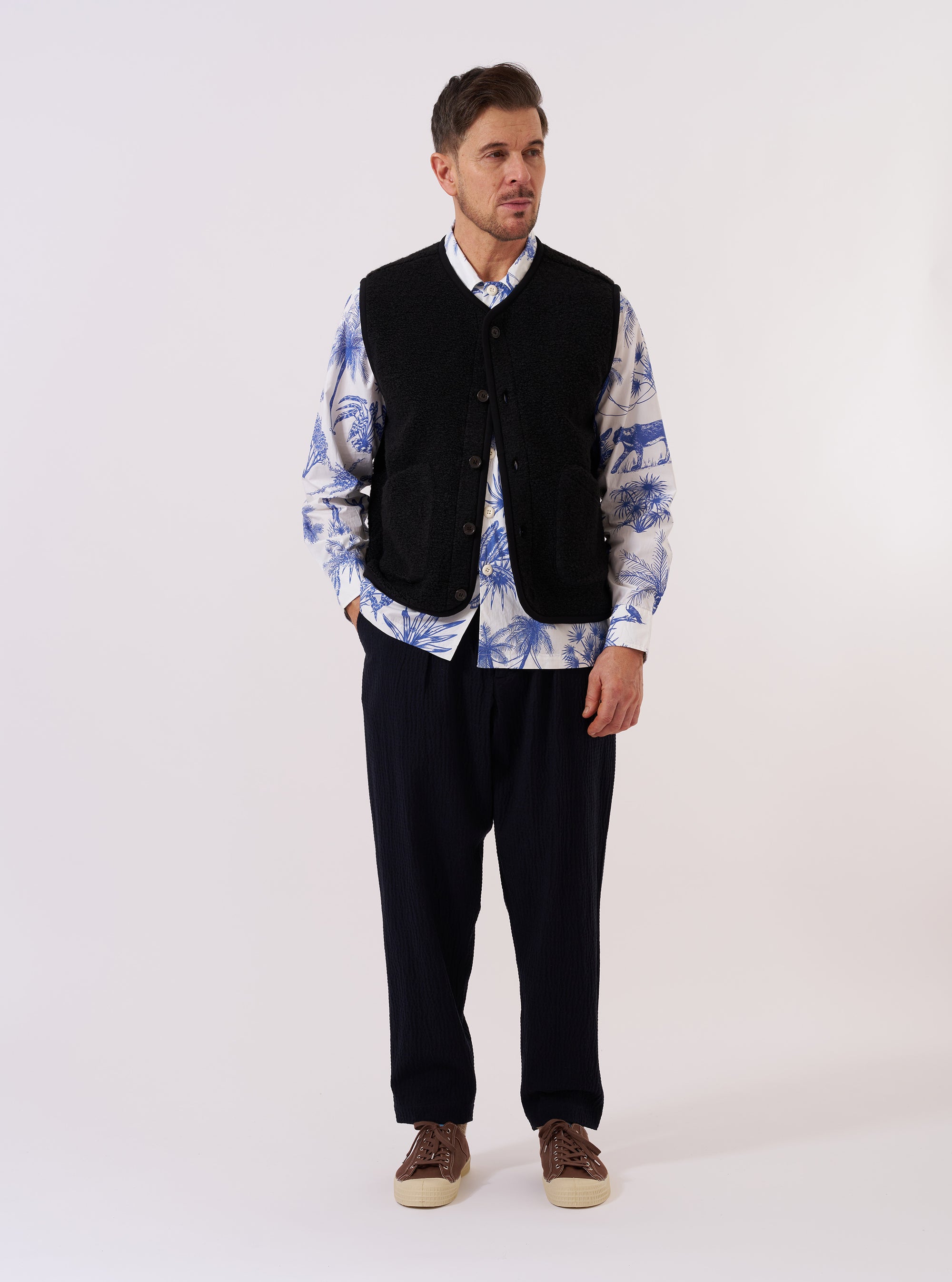 The Black Alvar Fleece Lancaster Gilet is shown as a flat lay against a plain white background. The gilet features a textured, fuzzy black fleece fabric, a rounded shawl collar, and a central button-down closure. It includes two large patch pockets at the waist and a single patch pocket on the left chest.