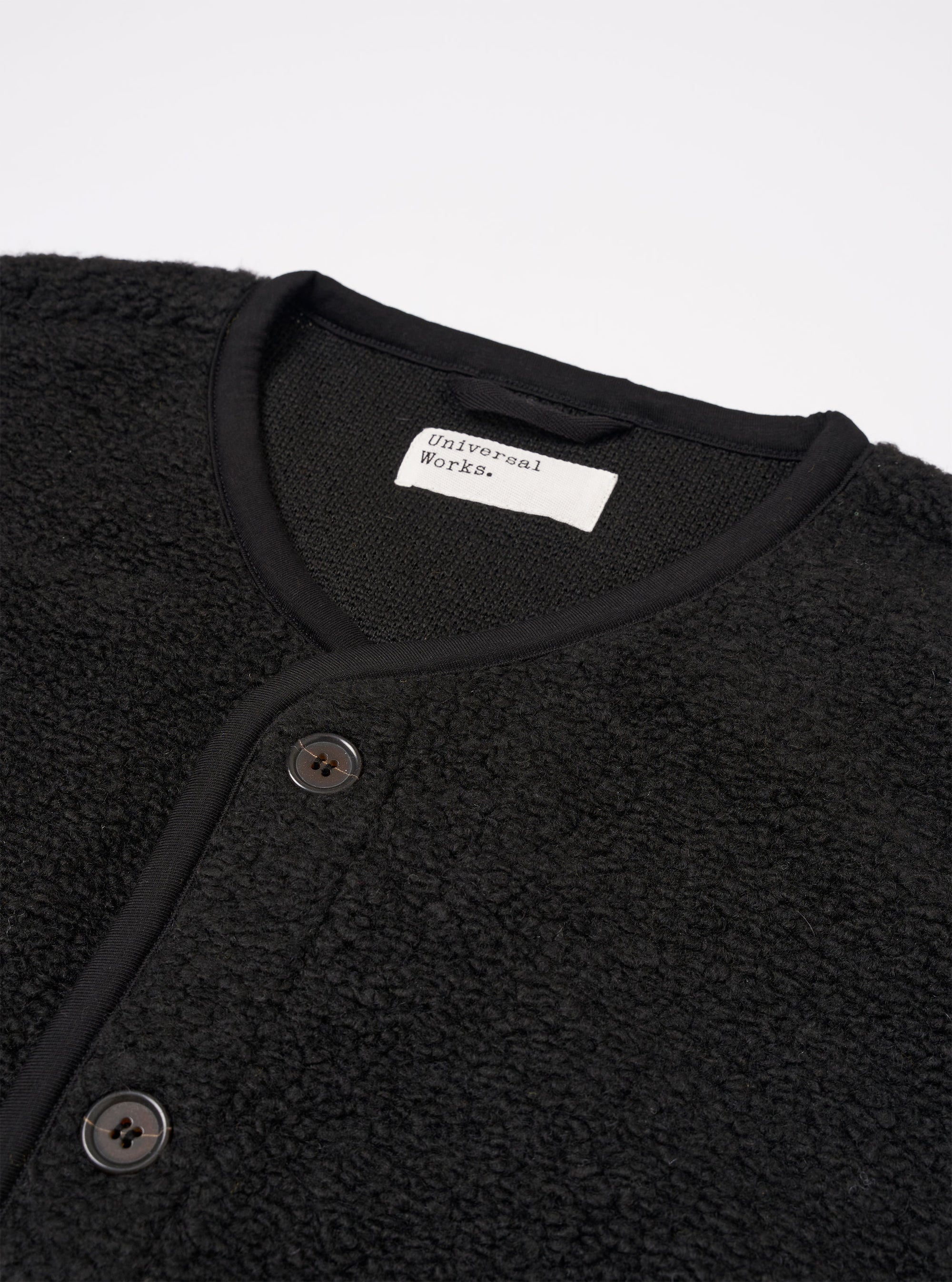The Black Alvar Fleece Lancaster Gilet is shown as a flat lay against a plain white background. The gilet features a fuzzy black fleece texture, a central button-down front closure, and a rounded shawl-style collar. It includes two large patch pockets at the waist and a single patch pocket on the left chest.