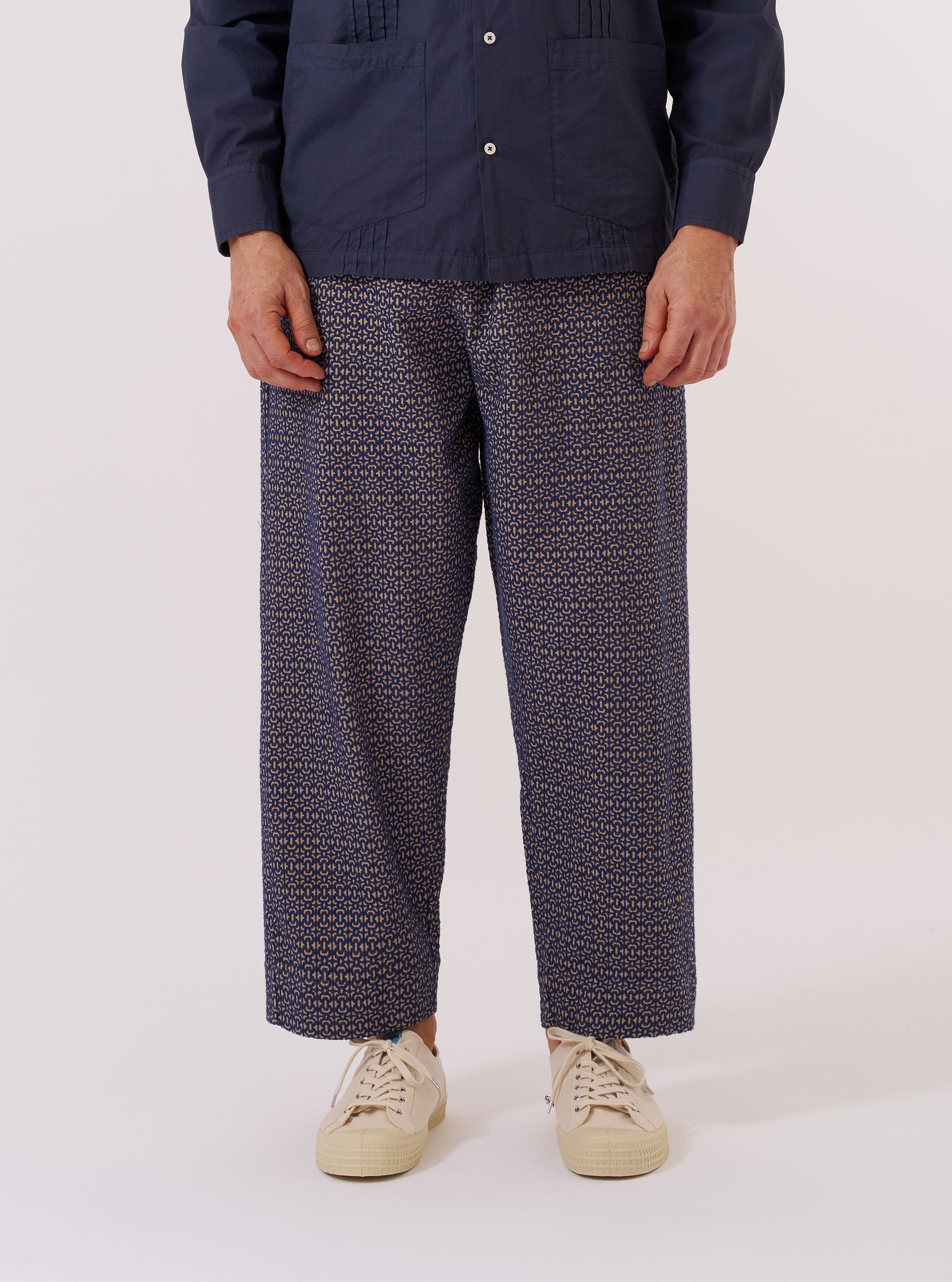 A model wears the Navy Konos Cotton Judo Pant against a plain white background. The trousers feature a loose, relaxed fit, an elasticated waistband with a drawstring, and a distinctive wrap-front design. The fabric is a navy blue cotton with a subtle textured pattern. The model is shown from the waist down, paired with white socks and dark shoes.