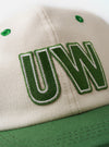 The Ecru/Green Canvas Baseball Hat is displayed as a flat lay against a plain white background. The cap features a light ecru crown with a contrasting green peak. It is constructed from a durable canvas fabric and includes tonal stitching and a curved brim.