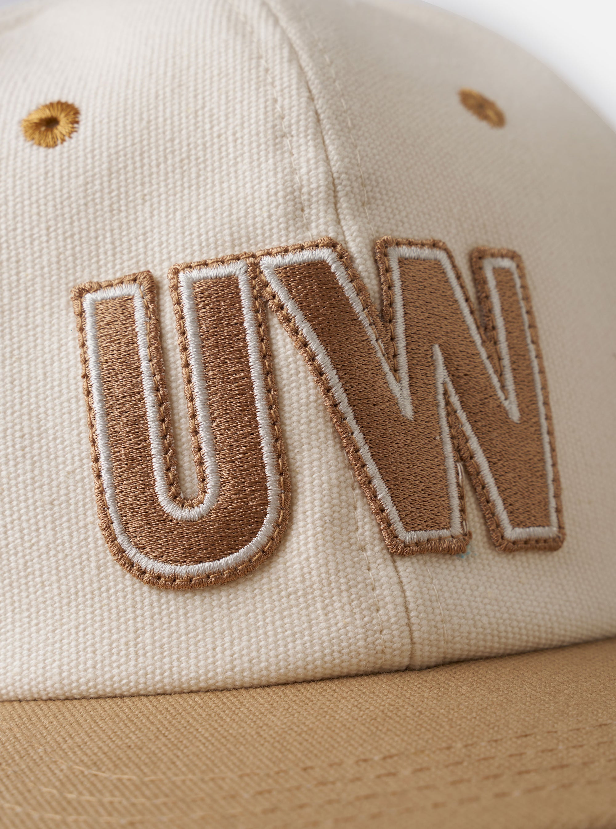 The Ecru/Sand Canvas Baseball Hat is shown in a detail view as a flat lay against a plain white background. The image highlights the adjustable fabric strap at the back with a metal slider and the clean stitching of the six-panel construction. The interior shows a tonal ecru lining and a woven brand label.
