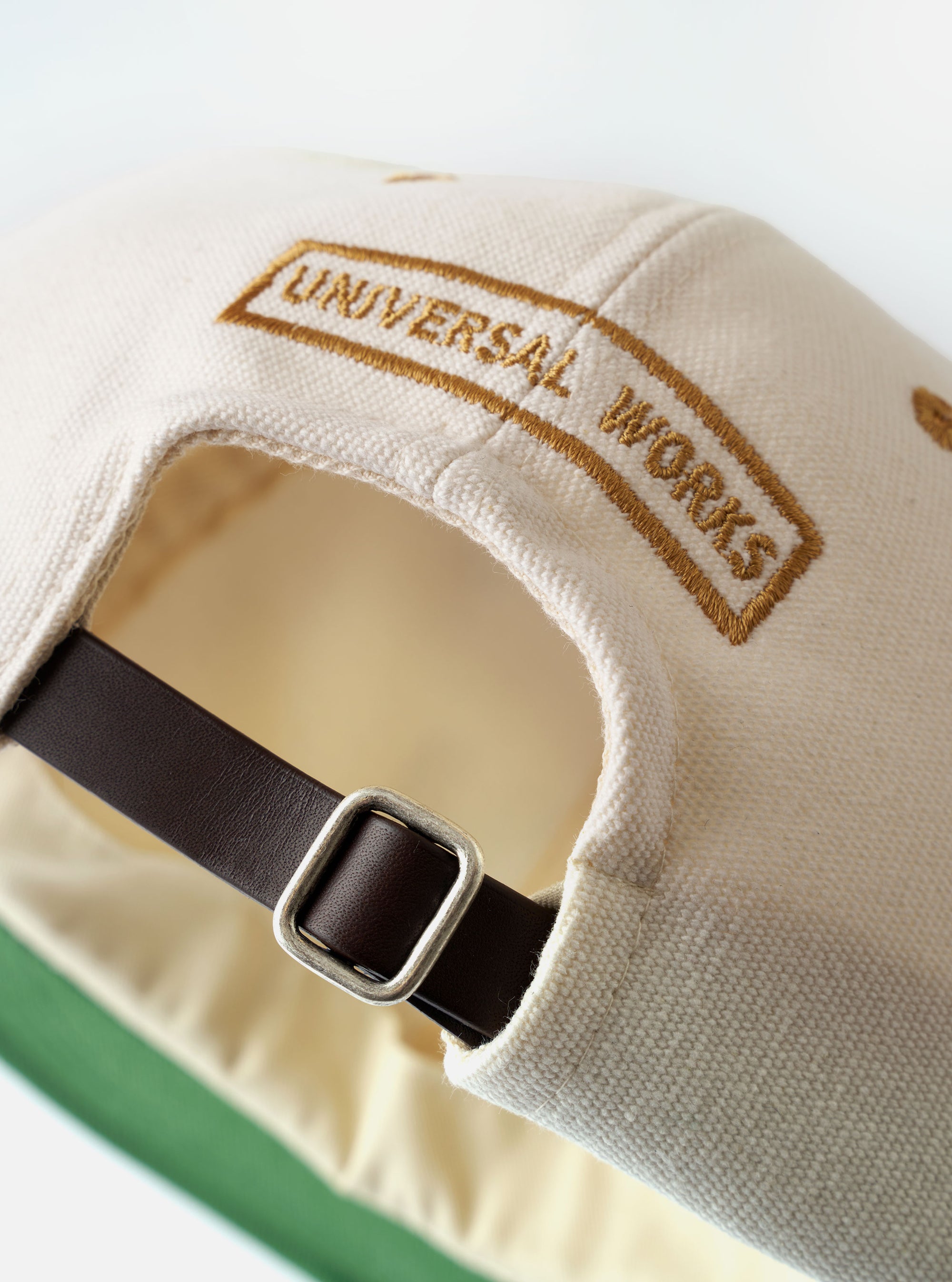 The Ecru/Sand Canvas Baseball Hat is shown as a flat lay against a white background. The hat features a six-panel construction in ecru canvas with a contrasting sand-colored wide peak and tonal eyelet details for ventilation. The fabric has a visible heavy canvas texture.