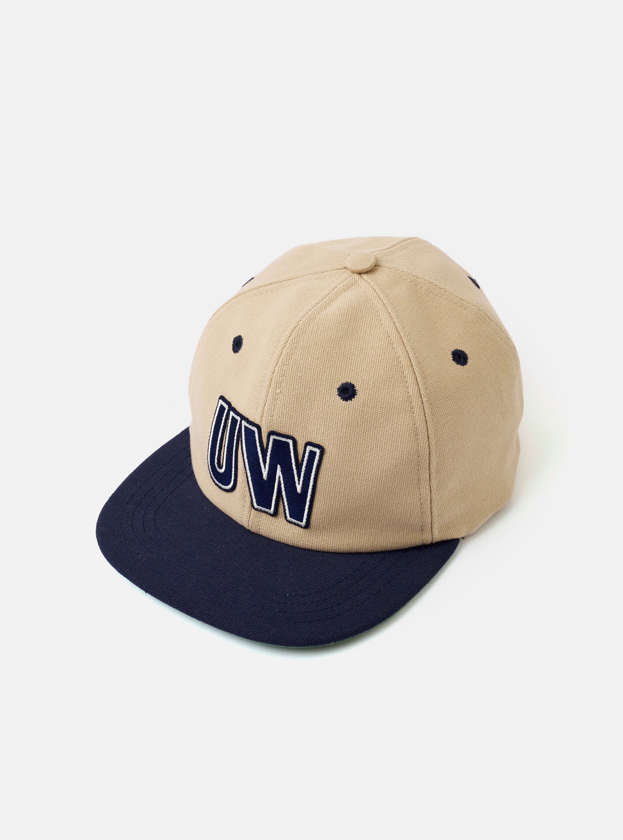 The Sand/Navy Canvas Baseball Hat is shown from a rear angle as a flat lay against a plain white background. The hat features a sand-colored canvas crown with a contrasting navy blue adjustable strap and a navy blue peak. Two embroidered eyelets are visible on the rear panels.