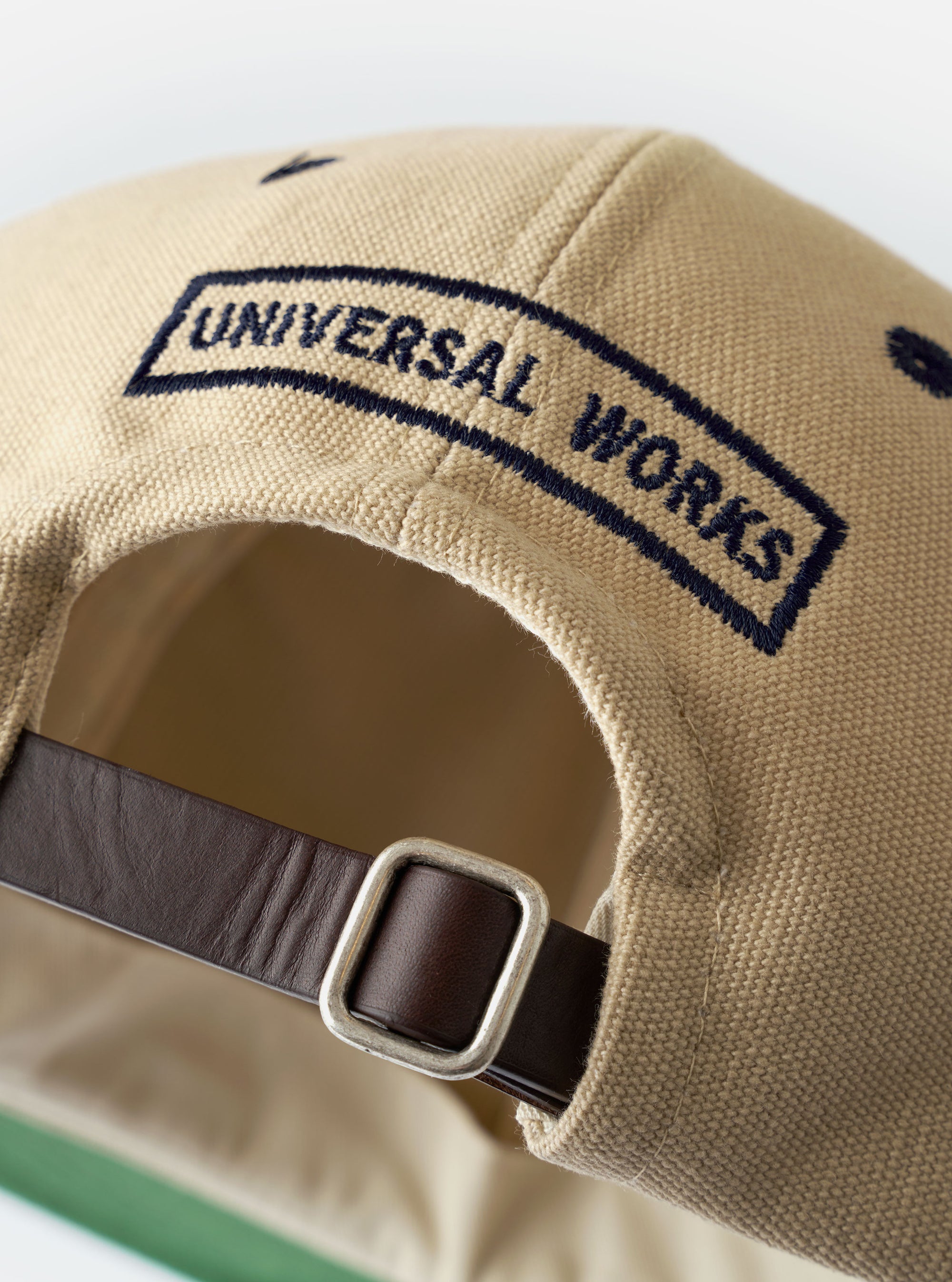 The Sand/Navy Canvas Baseball Hat is shown against a plain white background. The hat features a sand-colored canvas crown and a contrasting navy blue curved brim. It is designed with a classic six-panel construction, a matching top button, and tonal stitched eyelets for ventilation.