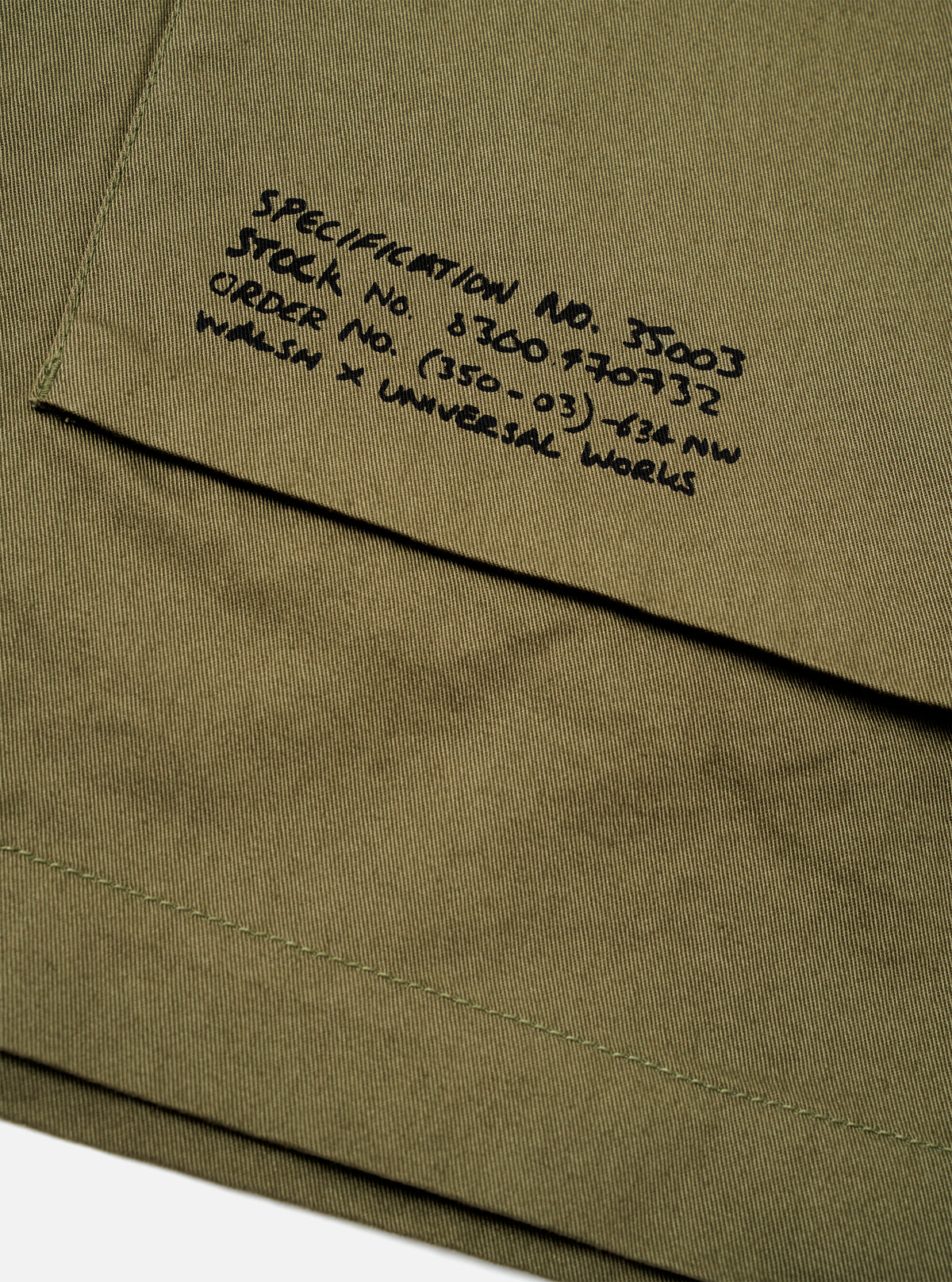 Rear view of a model wearing the Walsh x Universal Works Light Olive Twill Troopers Jacket against a plain studio background. The image displays the clean back panel construction, straight hem cut, and comfortable overshirt fit.