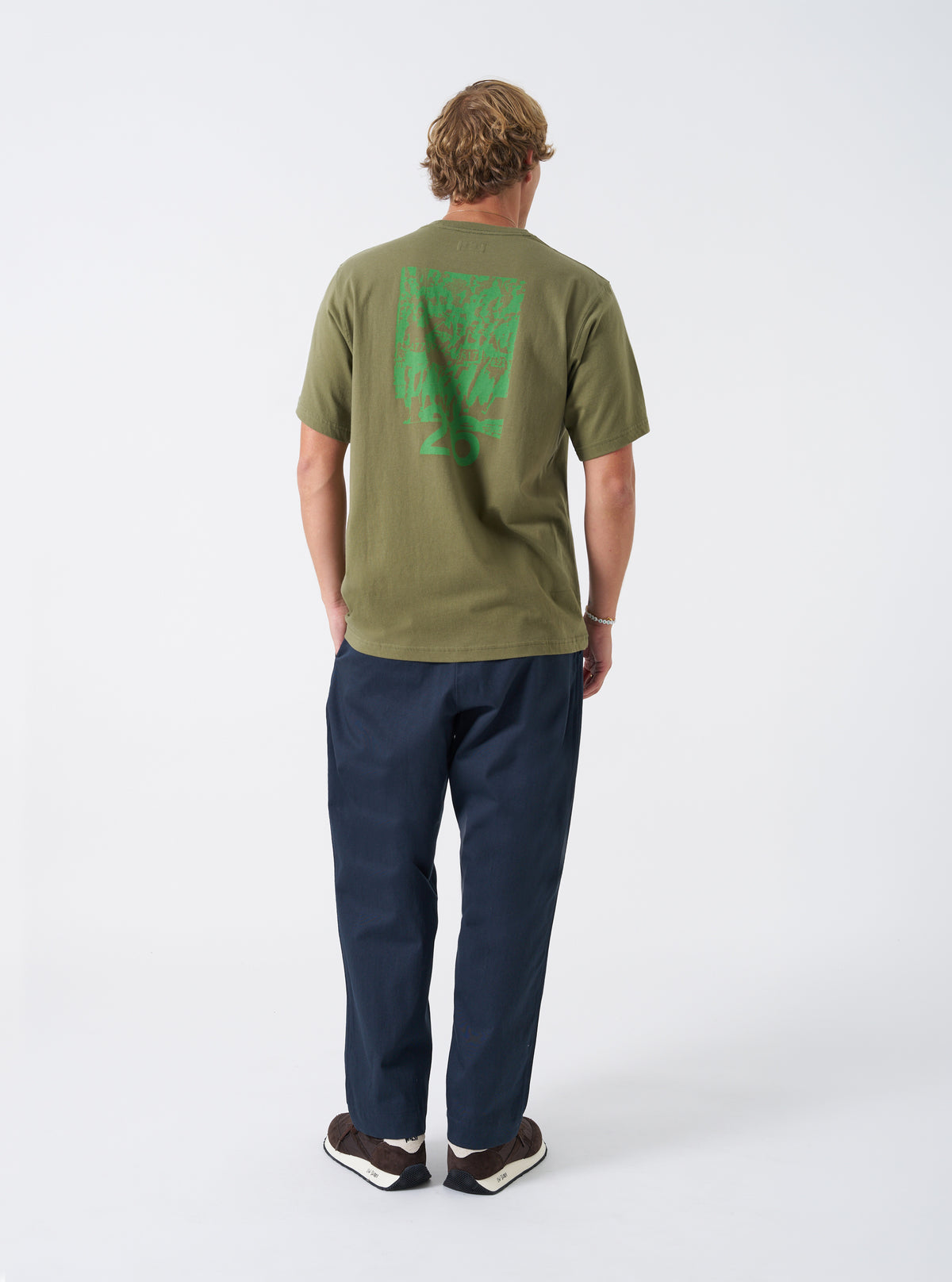 A model poses in the Walsh x Universal Works Olive Single Jersey T Shirt against a plain backdrop. The perspective shows the fit across the chest, shoulder alignment, hem, and rich olive green single jersey material.