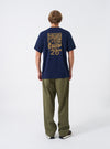 A model presents the Walsh x Universal Works Navy Single Jersey T Shirt against a plain studio background. The alternative view focuses on the relaxed fit across the chest, shoulders, tidy hemline, and deep navy colorway.