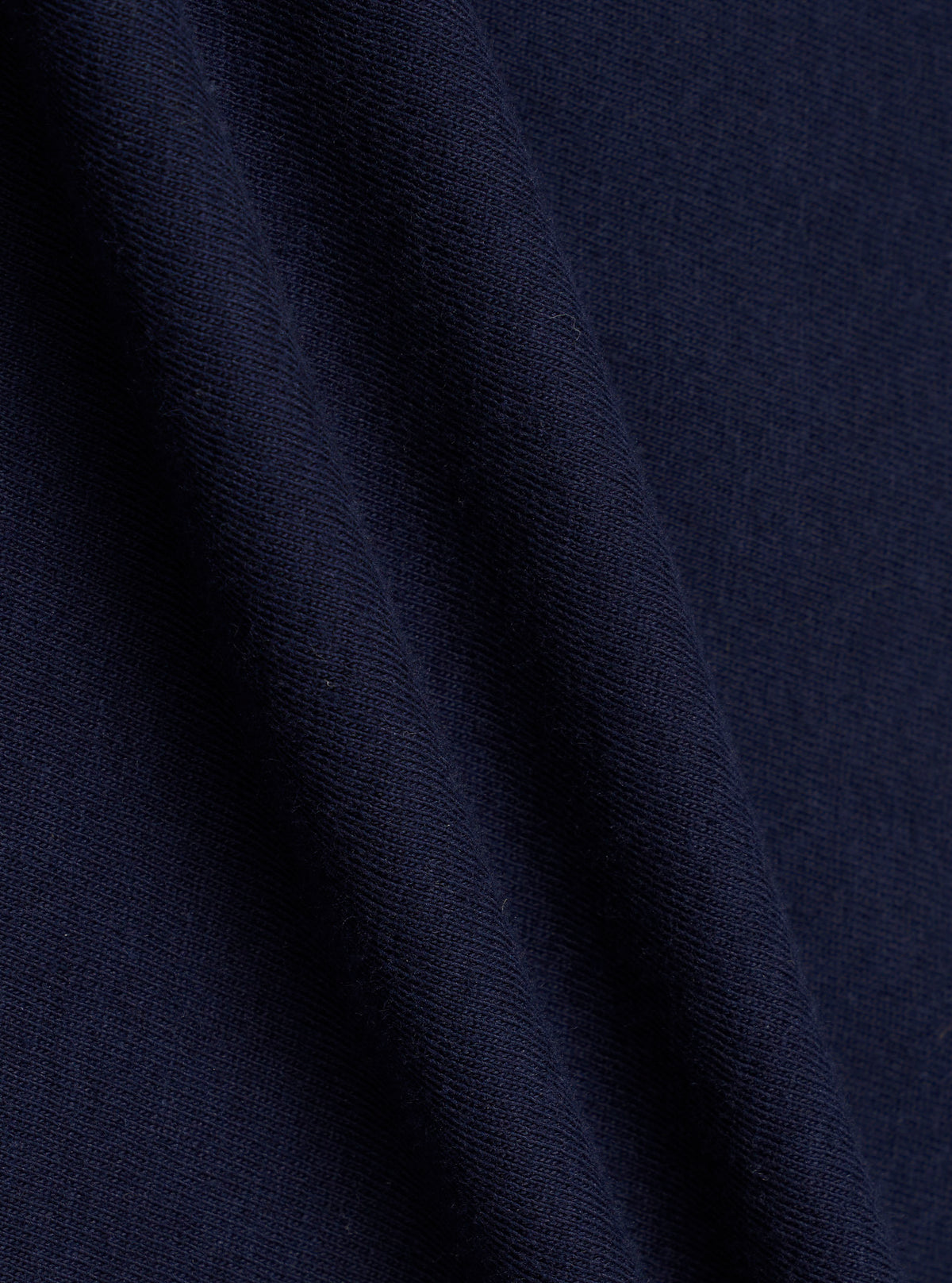 A swatch image showing a close-up detail of the Walsh x Universal Works Navy Single Jersey T Shirt fabric against a plain white backdrop. The shot highlights the fine knit pattern, soft texture, and solid navy blue colorway.
