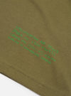 A close-up shot focusing on the collar and chest graphics of the Walsh x Universal Works Olive Single Jersey T Shirt against a plain background. The image showcases the detailed stitching, graphic print, and olive jersey fabric.