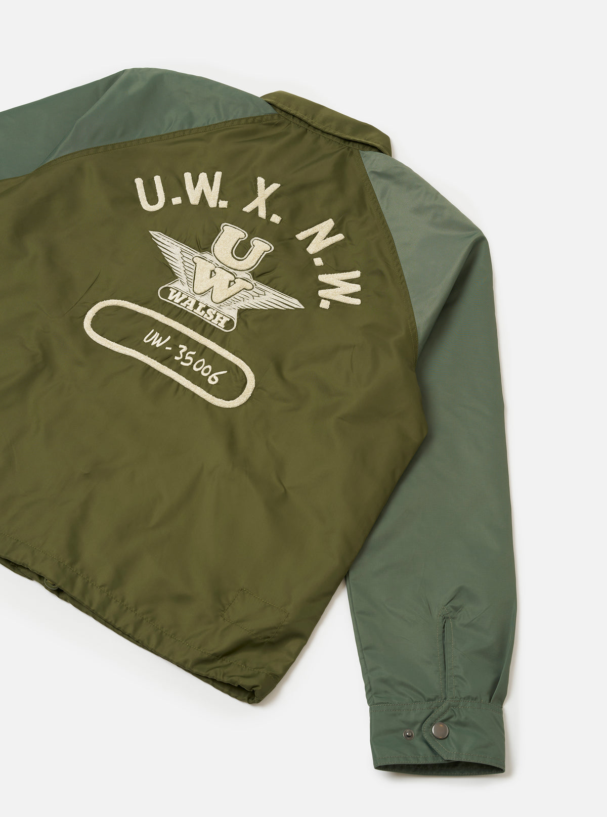 Rear view of the Walsh x Universal Works Olive Flight Nylon Club Coach Jacket on a plain backdrop. The image emphasizes the smooth back panel, neat shoulder seams, straight hemline, and rich olive green flight nylon construction.