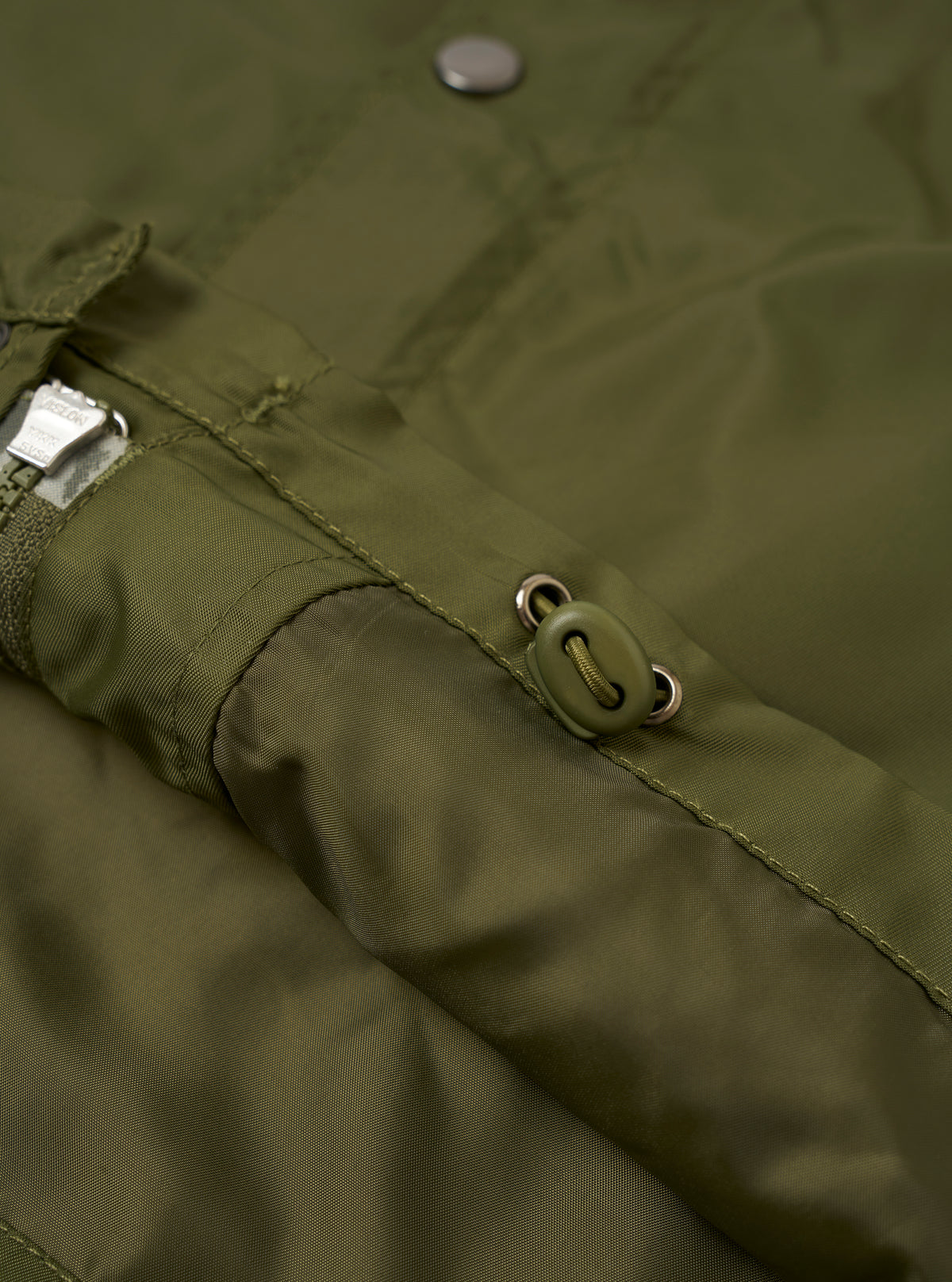 Back view of the Walsh x Universal Works Olive Flight Nylon Club Coach Jacket shown against a clean white backdrop. The design highlights a straight hemline, neat shoulder seams, and smooth olive green flight nylon material.