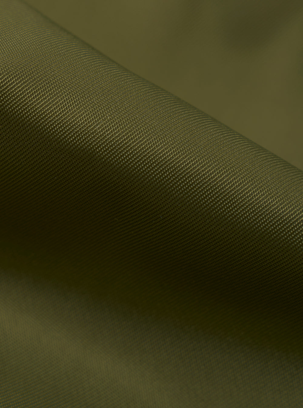 Extreme close-up shot of the Walsh x Universal Works Olive Flight Nylon Club Coach Jacket fabric. The image focuses on the fine weave texture, smooth olive green polyamide material, precise stitching, and subtle surface sheen.
