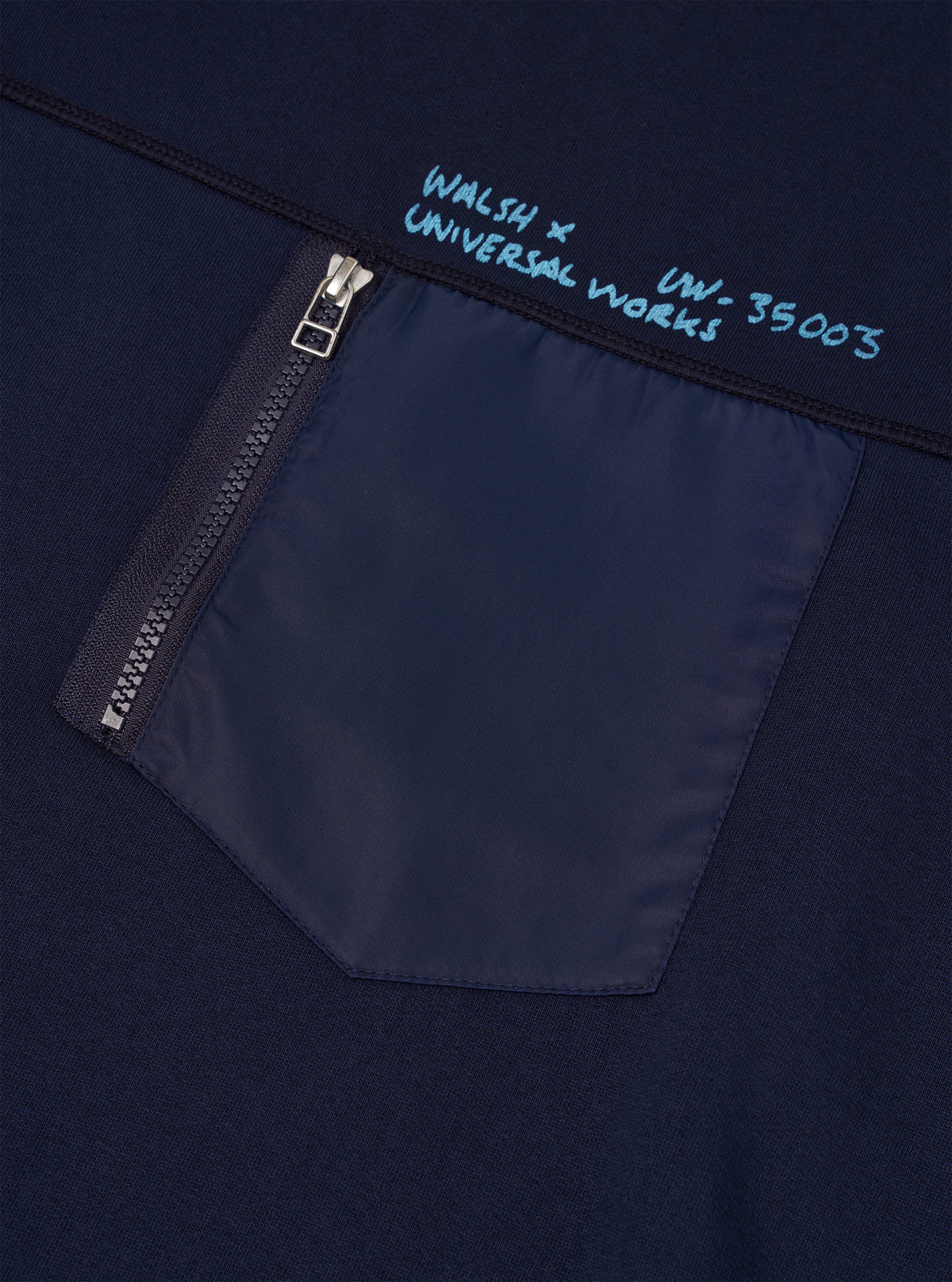 Detailed front shot of the Walsh x Universal Works Navy Brushback Sweat Panelled Loose Sweatshirt against a off-white background. The image highlights the neck ribbing, precise stitching across chest panels, and navy fabric texture.
