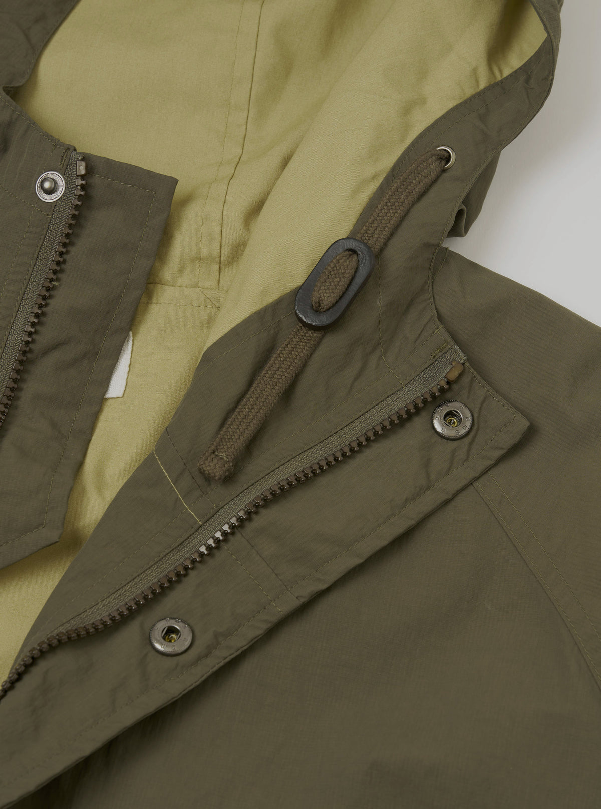A detailed product shot of the Olive WR Recycled Nylon Peak Parka set against a plain light studio background. Prominent features highlight the durable nylon fabric texture, hood construction, and clean rear seam stitching.