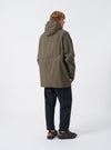 A male model stands against a plain neutral backdrop wearing the Olive WR Recycled Nylon Peak Parka. The photo highlights the back panel silhouette, protective hood, comfortable cut, and mid-length parka hem.