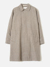 Taupe dogtooth check Stan Coat by Universal Works, laid flat on a light grey seamless backdrop. The longline coat features a soft point collar, concealed front placket, long sleeves with plain cuffs, two large patch pockets at the hip, and a relaxed oversized silhouette. The woven fabric shows a tan, navy and cream dogtooth pattern.