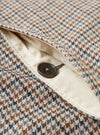 Close-up detail of the taupe dogtooth Stan Coat. A dark brown four-hole button sits on a cream woven lining visible through an open chest pocket. The outer fabric shows a multicolour dogtooth weave in taupe, brown, navy and grey. Shot on a plain white studio backdrop.