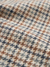 Close-up of the taupe Lester Dogtooth Stan Coat fabric, showing a woven dogtooth check pattern in cream, rust brown, navy and grey. The woollen textile has a lightly textured, hairy surface with visible yarn construction. The fabric is gathered into soft folds, highlighting its weight and drape.