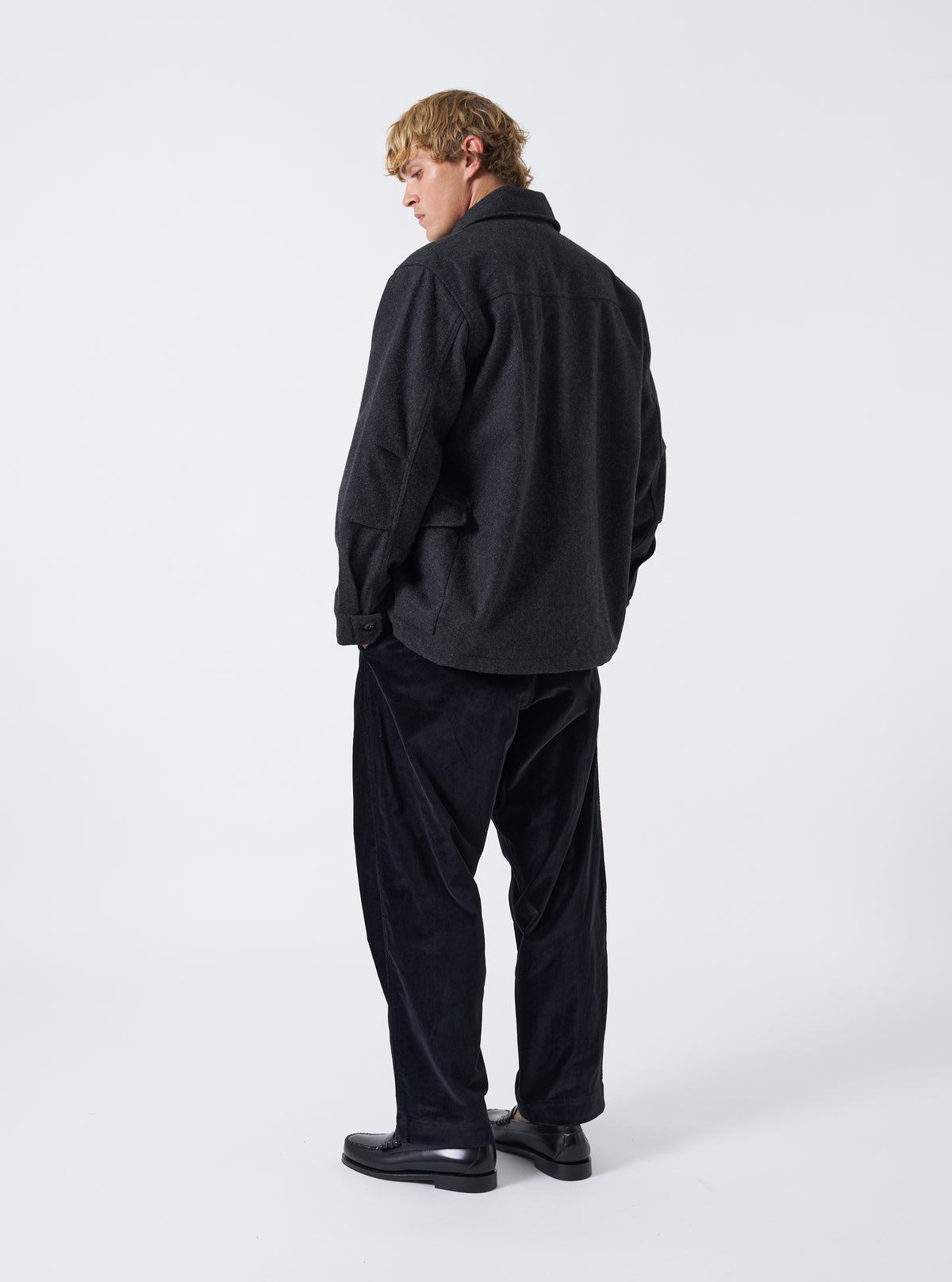 A male model stands against a clean neutral backdrop wearing the Grey Marl Mowbray Heavy Duty Jacket. The image showcases the relaxed jacket silhouette, grey marl wool texture, side pockets, and durable build.