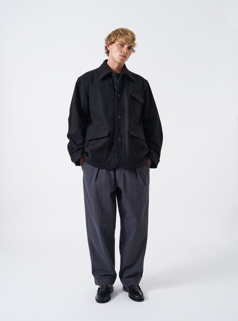 A male model wears the Black Mowbray Heavy Duty Jacket against a plain studio background. The front view highlights the rich black wool-blend material, structured collar, buttoned placket, and utility chest pockets.