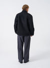 A male model stands against a neutral studio backdrop wearing the Black Mowbray Heavy Duty Jacket. The shot displays the back profile, heavy wool-blend texture, comfortable fit, and clean shoulder seams.