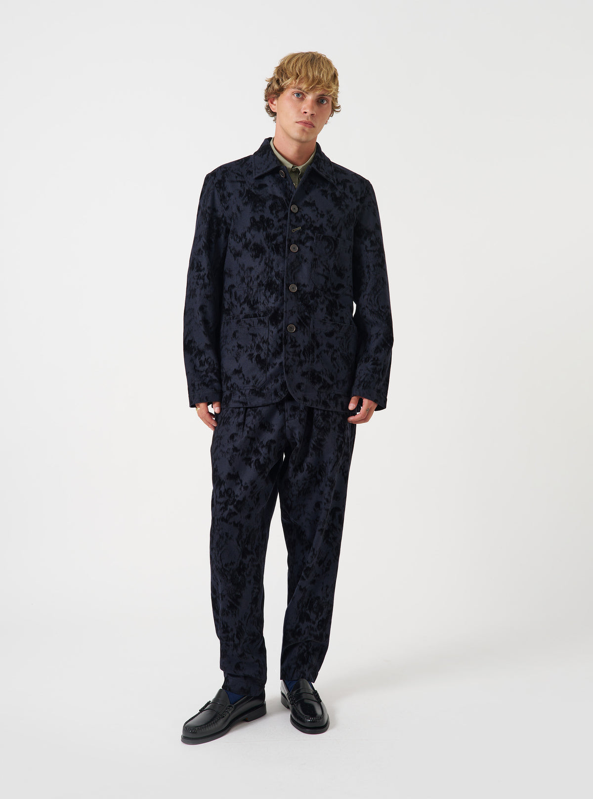 A male model stands against a plain neutral background wearing the Black Be Bop Wool Mix OG Bakers Chore Jacket. The studio shot highlights the dark wool blend, button front, classic collar, and spacious patch pockets.