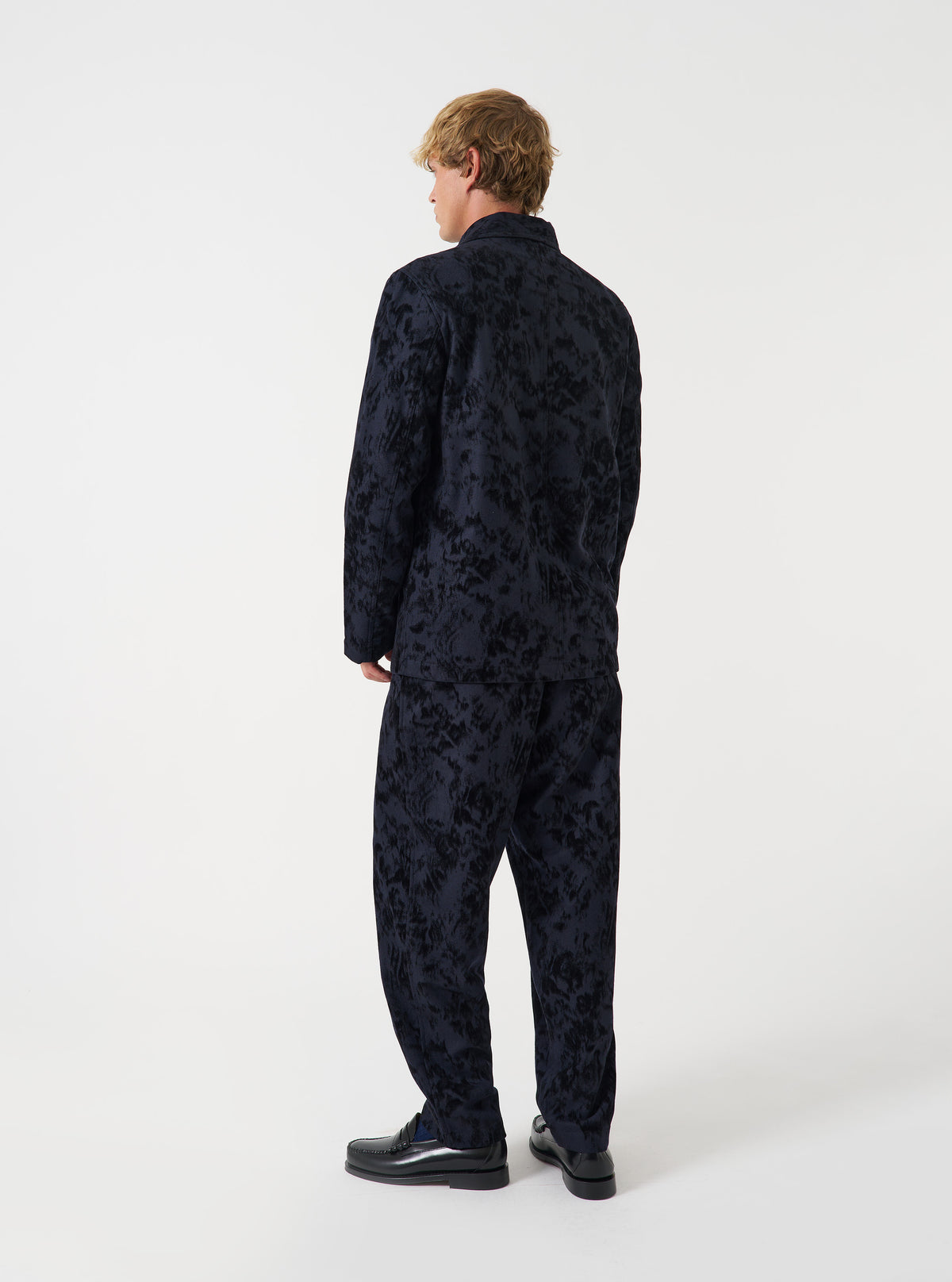 A model poses in a studio setting against a light backdrop wearing the Black Be Bop Wool Mix OG Bakers Chore Jacket. The photograph displays the fit, structured shoulders, buttoned placket, and deep utility pockets.