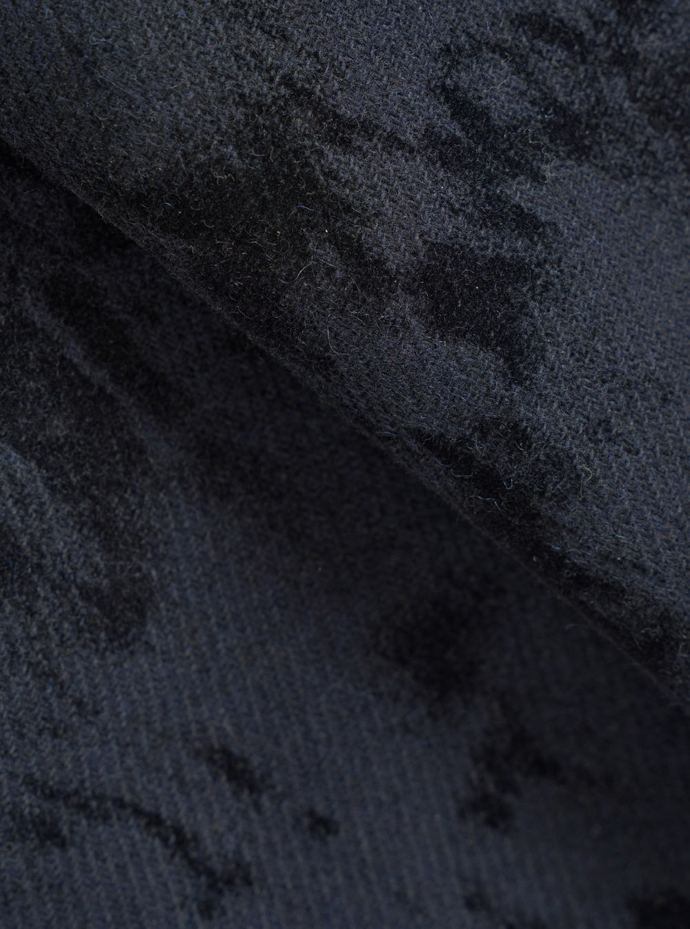 Close-up of the navy and black wool mix fabric of the Be Bop OG Bakers Chore Jacket, showing a tonal camo-style jacquard pattern. The textured, slightly brushed knit surface reveals depth and variation in colour across the folded fabric. No model or background visible.