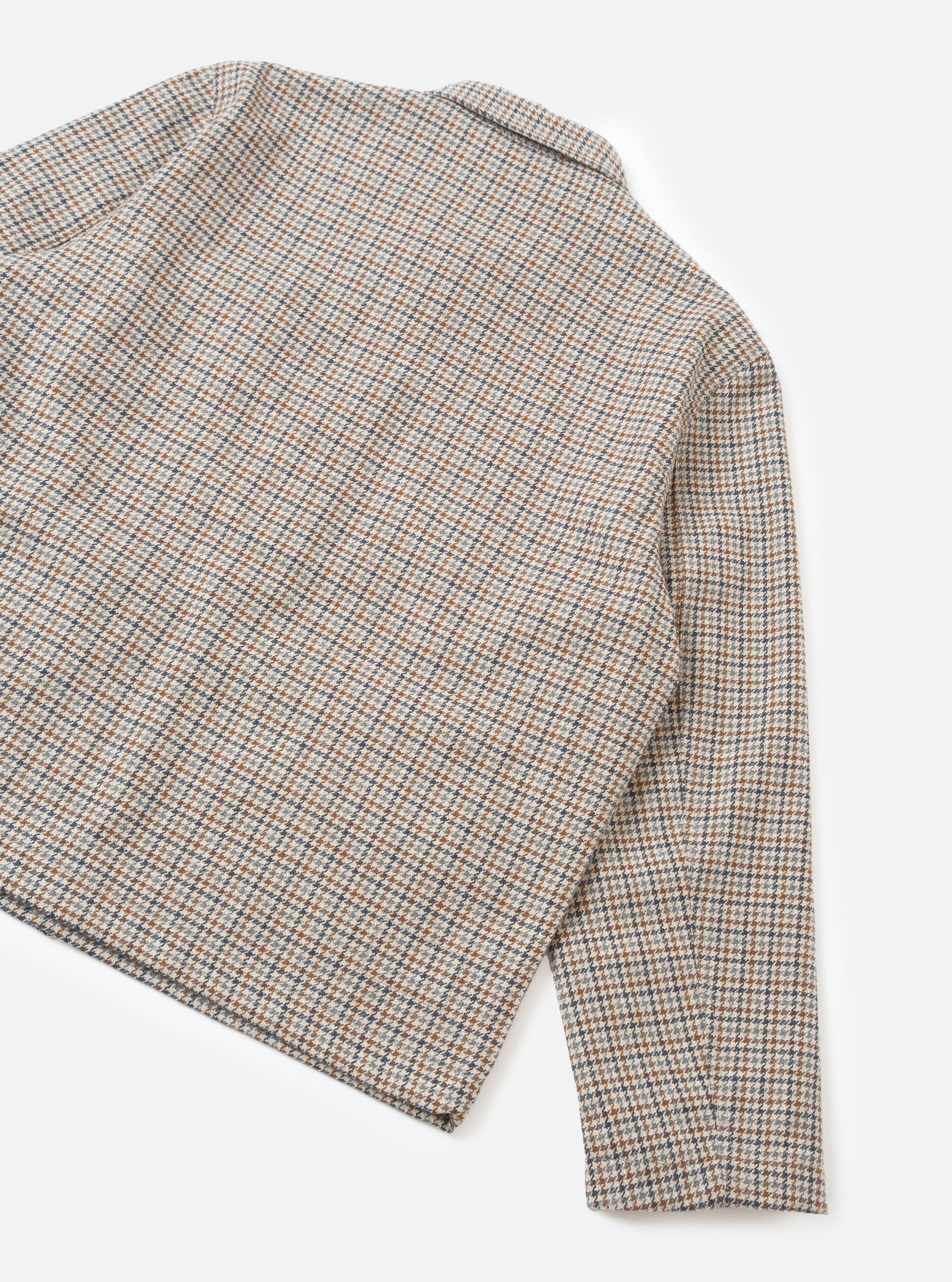 Flat lay of the taupe Lester Dogtooth Franck Jacket on a white studio backdrop, showing the upper body and one sleeve. The fabric features a multicolour dogtooth weave in taupe, tan, grey and navy. A spread collar is visible at the top. The unfinished cuff is shown at the sleeve hem.