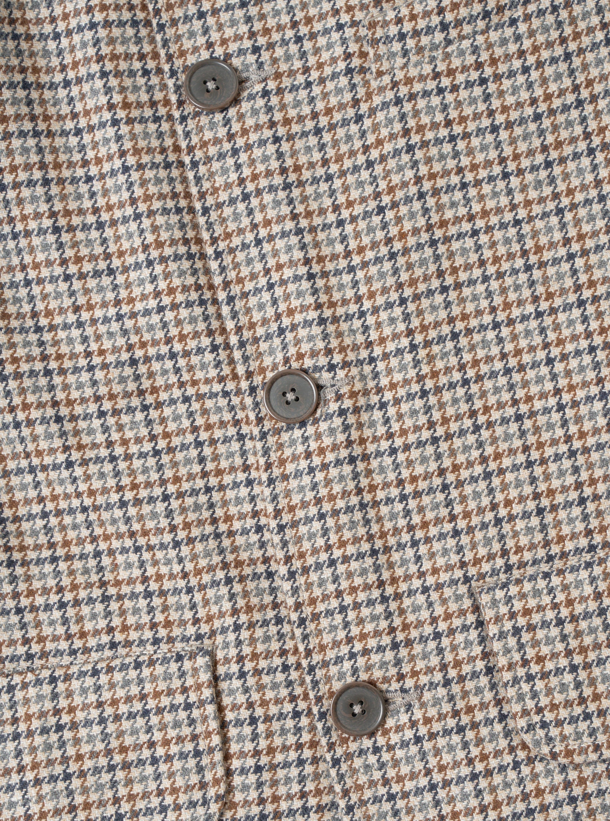 Close-up of the Taupe Lester Dogtooth Franck Jacket, showing the buttoned front placket with three visible grey four-hole buttons. The fabric features a multicolour dogtooth weave in taupe, tan, navy and grey. A welt pocket is visible at the lower left. Plain white studio backdrop.