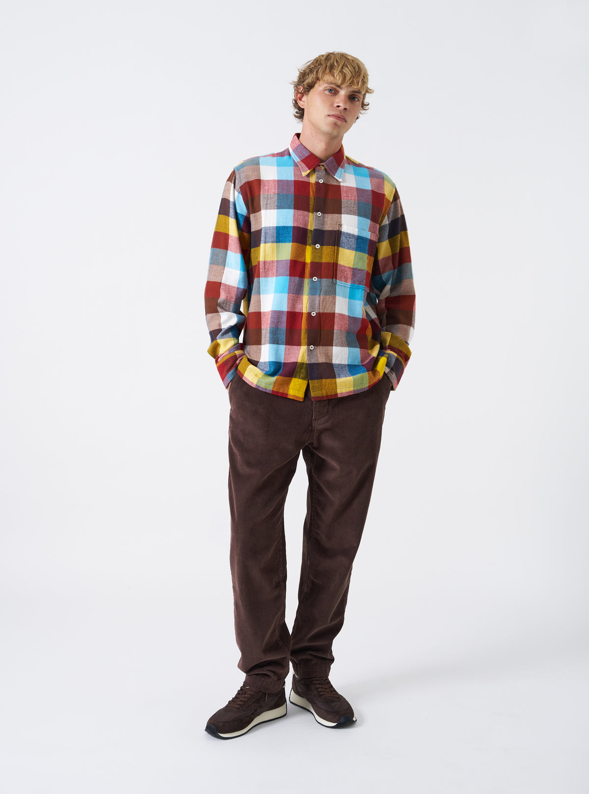 A male model wears the Multi Check Evans Check Lucky Shirt posed against a neutral studio backdrop. The shot showcases the shirt's relaxed fit, button-down front, chest pocket, and colorful check pattern.
